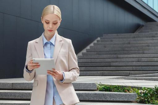 オフィスビルの外の階段を背にしてタブレットを持って立っているビジネスウーマン ビジネスウーマン,ビジネス,女性の写真素材