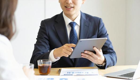 タブレットを使って説明する男性営業マン タブレットを使って説明する男性営業マンの写真