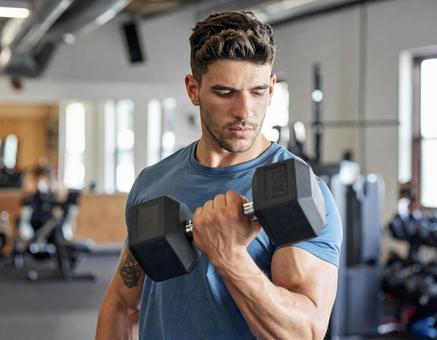 ジムでダンベル筋トレする男性 ジムでダンベル筋トレする男性の写真