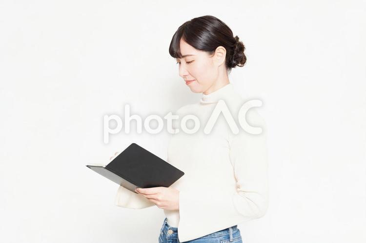 白背景の前に立って手帳にメモを書く女性 メモ,ノート,手帳の写真素材