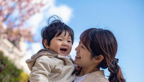 青空の下、子供を抱っこする母親の写真