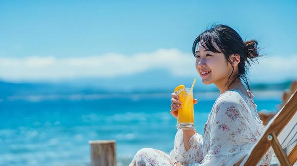 海辺でフルーツドリンクを楽しむ女性 海辺でフルーツドリンクを楽しむ女性の写真