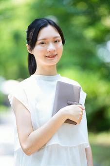 白いノースリーブワンピースの女性が本を胸に抱える 女性,本,手帳の写真素材