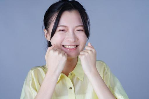 口元にこぶしを作って笑顔の黄色い服の女性 女性,笑顔,笑うの写真素材
