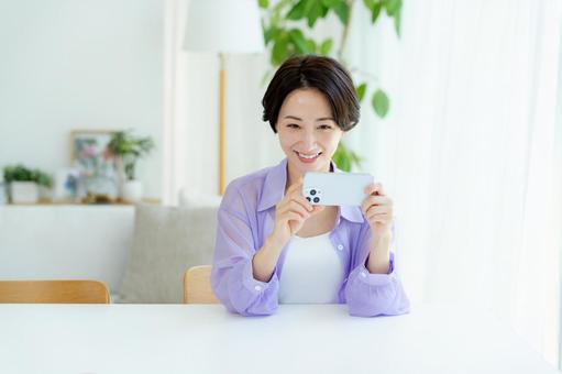 部屋でスマホを操作するミドル女性 スマホ,笑顔,女性の写真素材