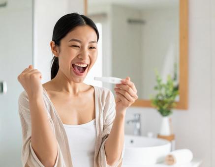 妊娠検査薬の陽性結果に歓喜する女性 妊娠検査薬の陽性結果に歓喜する女性の写真