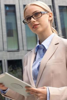 オフィスビルの外でタブレットを持って立つメガネを掛けたビジネスウーマン ビジネスウーマン,ビジネス,女性の写真素材