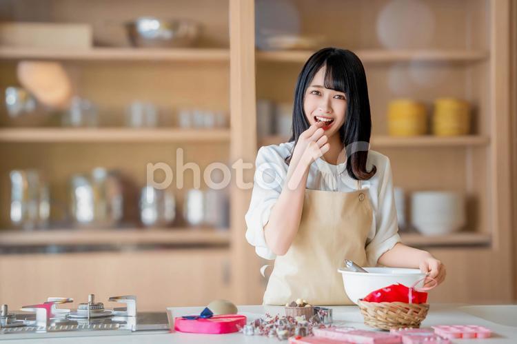 チョコをつまみ食いするエプロン姿の女性 バレンタイン,バレンタインデー,チョコの写真素材