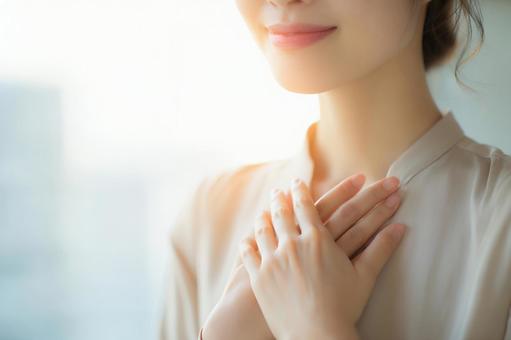 胸に手を当てて安心する女性 胸に手を当てて安心する女性の写真