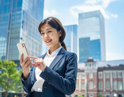 オフィス街でスマホを操作する女性社員 オフィス街でスマホを操作する女性社員の写真