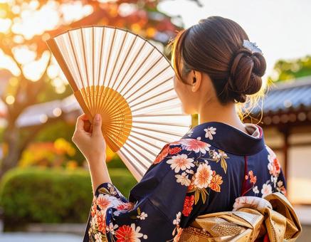夕日に輝く着物姿の女性と扇子の写真