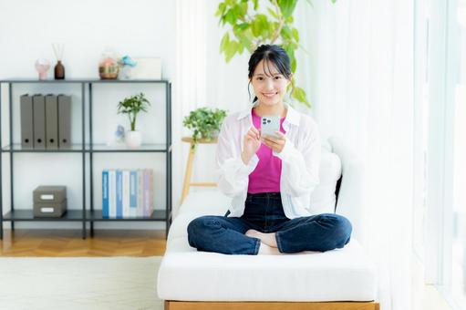 部屋でスマホを操作する若い女性 スマホ,笑顔,若い女性の写真素材