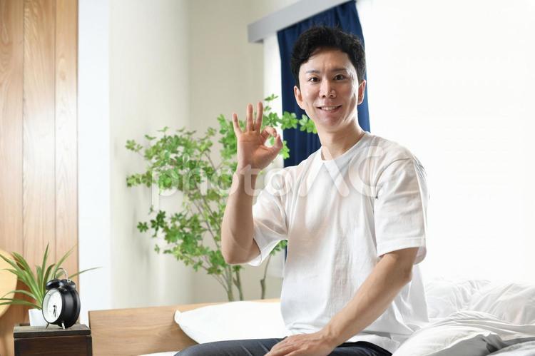 ベッドの上でOKをする若いアジア人男性 ベッド,男性,安眠の写真素材