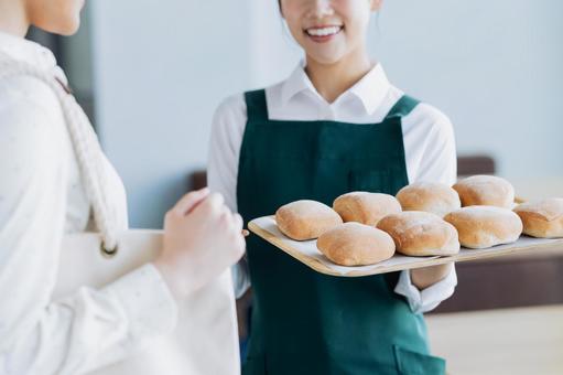 パンをすすめる若い女性の店員 パンをすすめる若い女性の店員の写真