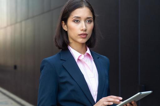 街なかでタブレットを使うスーツの女性 ビジネスウーマン,ビジネス,女性の写真素材
