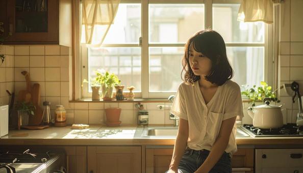 疲れた表情でキッチンに座る若い女性 疲れた表情でキッチンに座る若い女性の写真