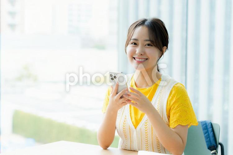 カフェでスマホを見る学生 スマホ,若い女性,笑顔の写真素材