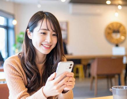 カフェでスマートフォンを操作する女性 カフェでスマートフォンを操作する女性の写真
