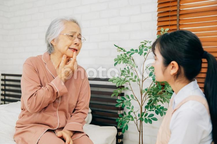痛がる高齢者女性とエプロン姿の女性（口・あご） 口,ドライマウス,唇の写真素材