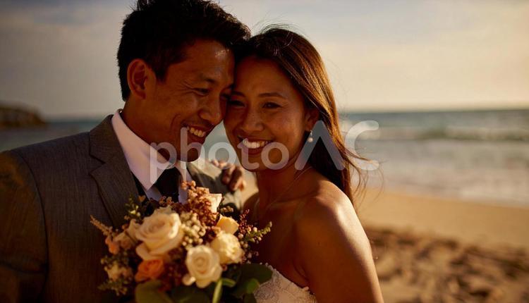 海辺でブーケを持ち顔を見合わせる新郎新婦 海,ウエディング,結婚の写真素材