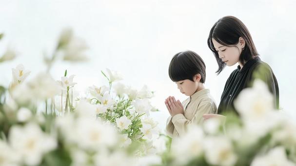 葬式や法事で祈る母と息子、白い花の写真