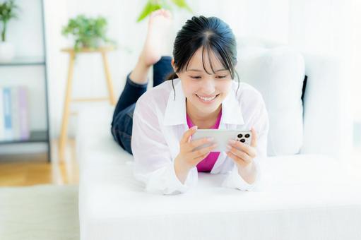 部屋でスマホを操作する若い女性 部屋でスマホを操作する若い女性 スマホ,若い女性,笑顔の写真素材