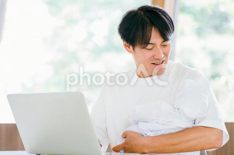 赤ちゃんを抱きながら仕事する男性 テレワーク,育児,リモートワークの写真素材
