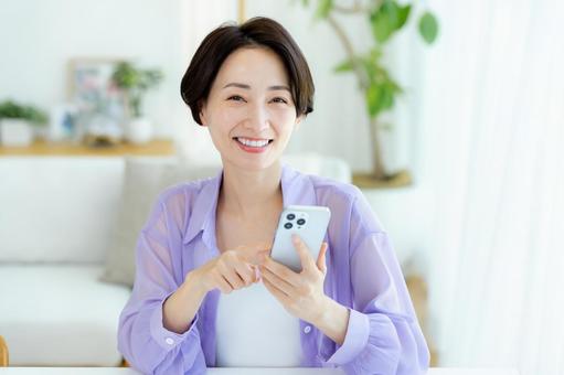 部屋でスマホを操作するミドル女性 部屋でスマホを操作するミドル女性 スマホ,笑顔,女性の写真素材