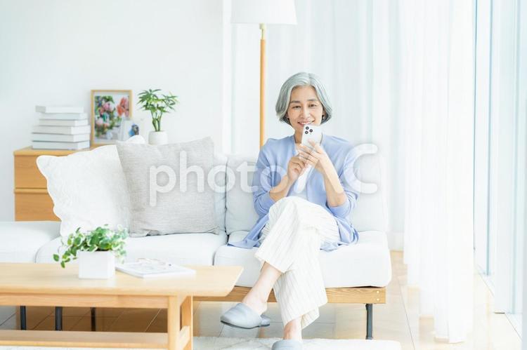 リビングでスマホを操作するシニア女性 シニア,スマホ,笑顔の写真素材