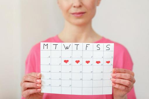 屋内で月経期間を示すカレンダーを手に持っっている女性の写真