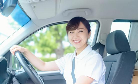 笑顔でハンドルを握る白いポロシャツの女性の写真