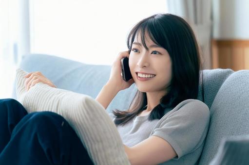 ソファに座ってスマホで話す笑顔の女性 女性,スマホ,スマートフォンの写真素材
