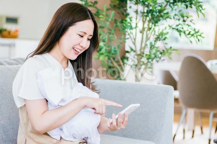 赤ちゃんを抱きながらスマホを使う女性 赤ちゃん,ママ,子育ての写真素材