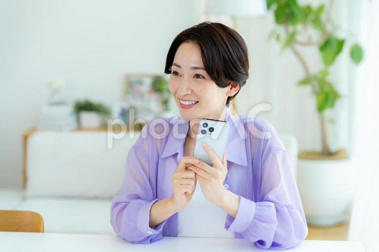 部屋でスマホを操作するミドル女性 スマホ,笑顔,女性の写真素材