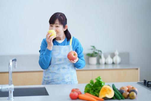 りんごの匂いを嗅ぐ中年女性とキッチンの健康的な暮らし りんごの匂いを嗅ぐ中年女性とキッチンの健康的な暮らしの写真