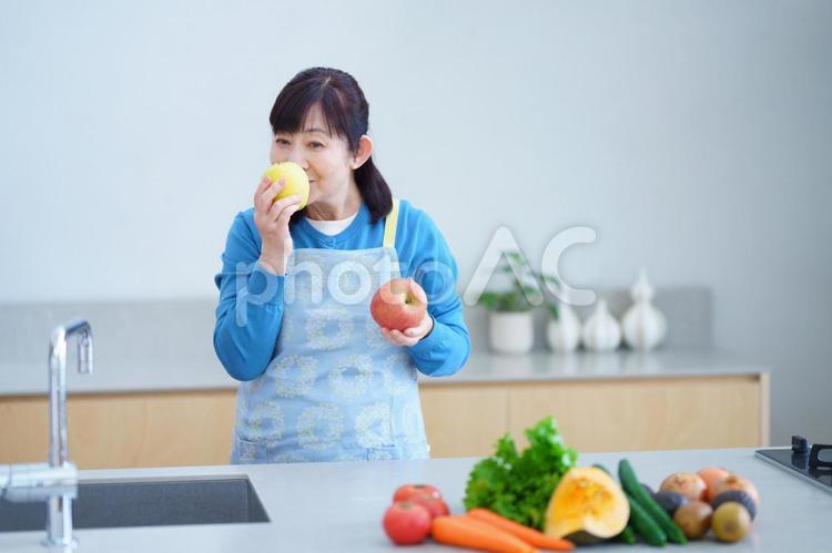 りんごの匂いを嗅ぐ中年女性とキッチンの健康的な暮らし 主婦,家政婦,エプロンの写真素材