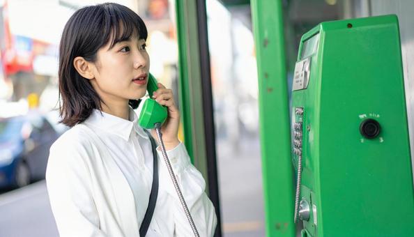 帯の通信障害で公衆電話を使う若い女性 帯の通信障害で公衆電話を使う若い女性の写真