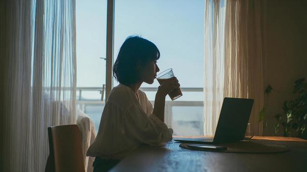 パソコンをしながら飲み物を飲む女性 パソコンをしながら飲み物を飲む女性の写真