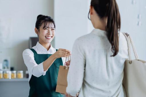 商品を渡す若い女性の店員 商品を渡す若い女性の店員の写真