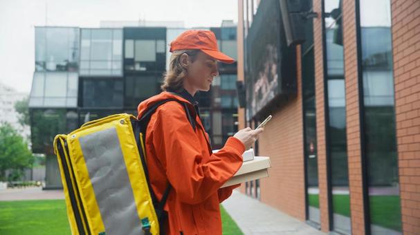 ピザ箱を抱えてスマートフォンを使うフードデリバリーの男性 配達,フードデリバリー,デリバリーの写真素材
