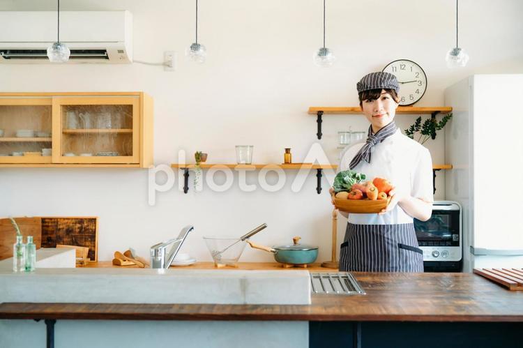 キッチンに立つコックコートを着た調理師（野菜・笑顔） 調理師,野菜,調理の写真素材
