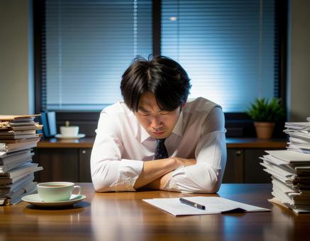 書類の山に囲まれて疲れる男性社員 書類の山に囲まれて疲れる男性社員の写真