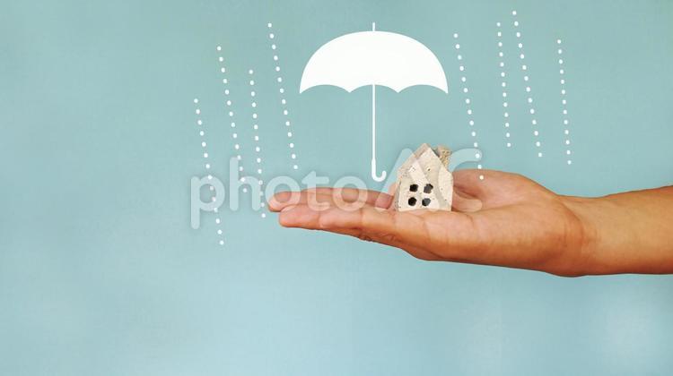 家小物を乗せる手と雨と傘マーク_青背景 家,傘,雨の写真素材