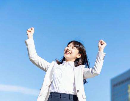 青空の下伸びをするビジネス女性・就活生の写真