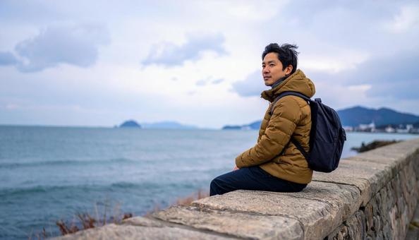 冬の空の下、一人旅を楽しみ石垣に座る男性 冬の空の下、一人旅を楽しみ石垣に座る男性の写真