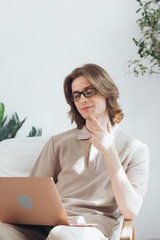 顎を触りながら膝の上のノートパソコンを使う若い男性 男性,外国人,欧米人の写真素材