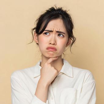 ベージュの背景で疑問を抱くアジア人女性 ベージュの背景で疑問を抱くアジア人女性の写真