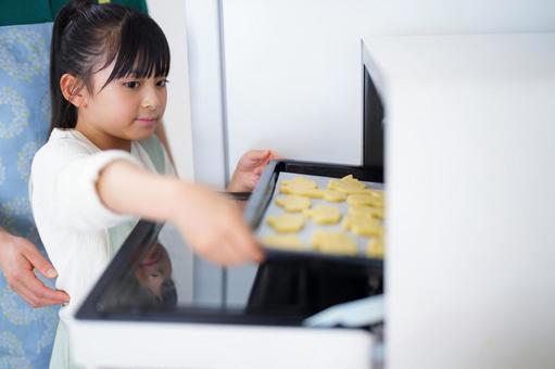 オーブンにクッキーを入れるエプロン姿の少女 女の子,日本人,クッキーの写真素材