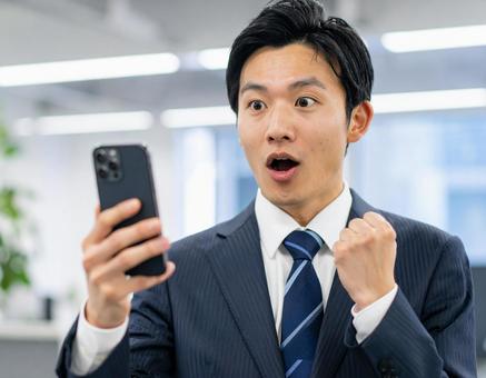 スマートフォンを見て驚くスーツ姿の男性の写真