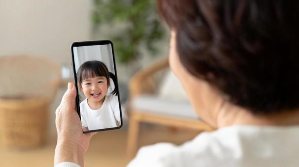 孫とテレビ電話をするおばあちゃん 孫とテレビ電話をするおばあちゃんの写真